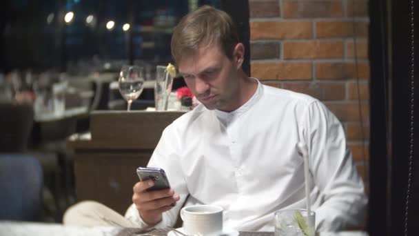 Mann som sjekker en mobiltelefon om natten i en restaurant. 4k, sløret bakgrunn – stockvideo