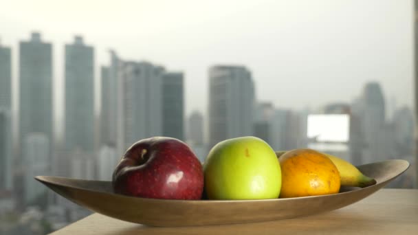 La main prend la pomme de l'assiette, contre la fenêtre avec vue sur les gratte-ciel. 4k, au ralenti — Video