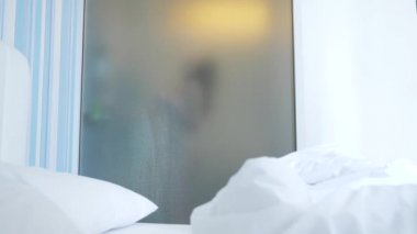4k, ağır çekim. Tanınmayan kız duş alır. biri yatak odası ve banyo arasında şeffaf duvarı baktığı. Bulanık cam arkasındaki kadın. Kadın banyoda.