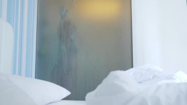 4k, ağır çekim. Tanınmayan kız duş alır. biri yatak odası ve banyo arasında şeffaf duvarı baktığı. Bulanık cam arkasındaki kadın. Kadın banyoda.