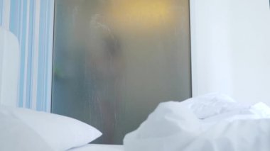 4k, ağır çekim. Tanınmayan kız duş alır. biri yatak odası ve banyo arasında şeffaf duvarı baktığı. Bulanık cam arkasındaki kadın. Kadın banyoda.