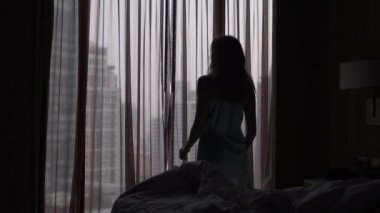 Bir kadın gökdelenler bakan bir pencere geliyor uykudan uyanır, perdeleri açar. ağır çekim. 4k