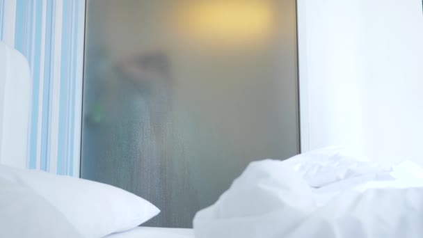 4k, rallenta. ragazza irriconoscibile si fa una doccia. qualcuno lo guarda attraverso il muro trasparente tra la camera da letto e il bagno. La donna dietro il vetro sfocato. Donna in bagno . — Video Stock