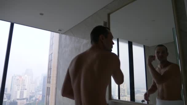 Un hombre guapo aplicando una navaja de afeitar en el baño con vista desde la ventana a los rascacielos. 4k, cámara lenta — Vídeos de Stock