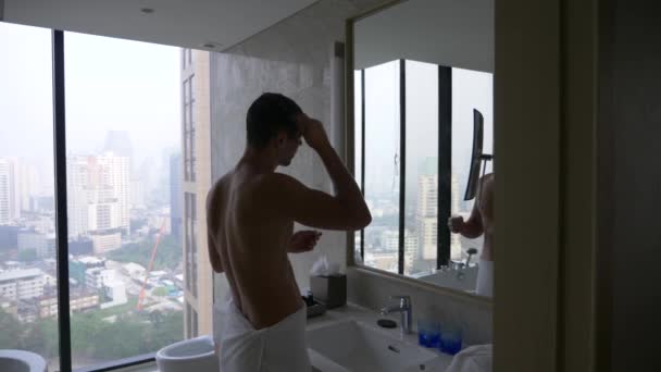 ハンサムな男は、高層ビルの窓からの眺め、バスルームの鏡の前で自分の髪を櫛します。4 k、スローモーション — ストック動画