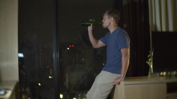 Bir adam bira evde yanında gökdelenler bakan panoramik bir pencere içiyor. İyi geceler, arka plan bulanıklık. 4k, ağır çekim — Stok video