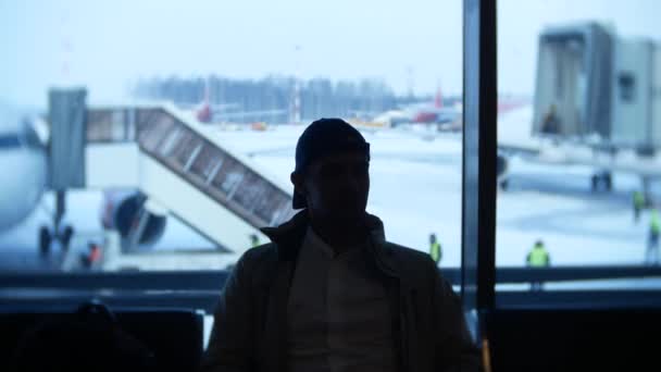 Αγνώστων στοιχείων άντρας περιμένει στο αεροδρόμιο μπροστά από ένα παράθυρο. 4k — Αρχείο Βίντεο