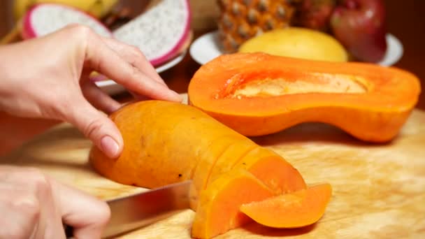 Frutas exóticas en la mesa. 4k, las manos de las mujeres preparan la papaya para la tabla de cortar — Vídeos de Stock