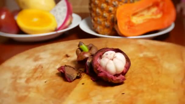Frutas exóticas na mesa. 4K. Mangostin gira na placa de corte — Vídeo de Stock