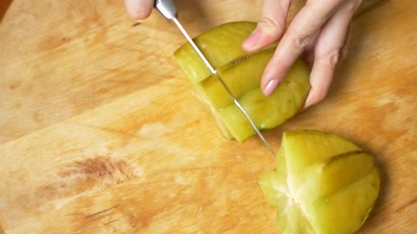 Exotiska frukter på bordet. 4k, kvinnliga händer skär en carambola med en kniv på en skärbräda, Slow motion — Stockvideo
