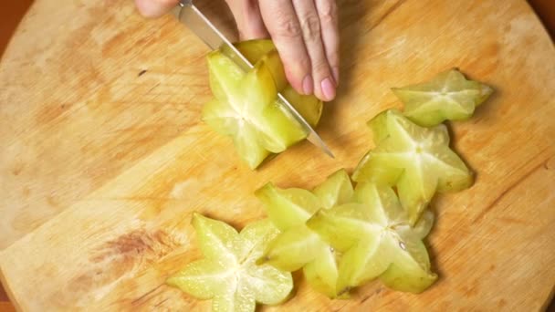 Frutas exóticas en la mesa. 4k, las manos femeninas cortan una carambola con un cuchillo en una tabla de cortar, cámara lenta — Vídeos de Stock