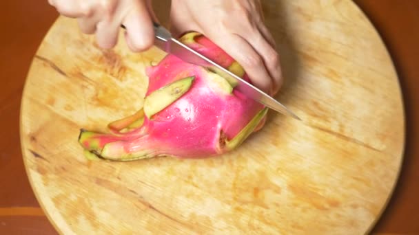 Exotische vruchten op de tafel. 4k, vrouwelijke handen een drakenfruit snijden met een mes op een snijplank in stukjes — Stockvideo