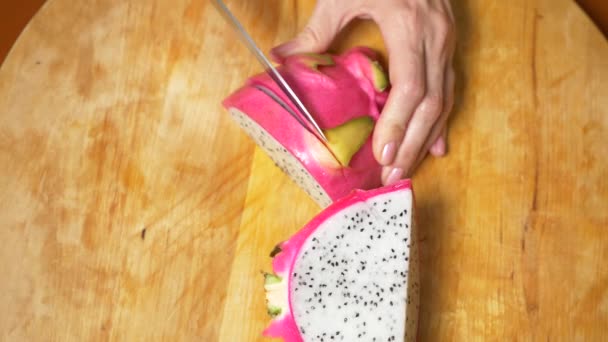Egzotycznych owoców na stole. 4k, kobiecych rąk cięcia dragonfruit z nożem na deska do krojenia na kawałki — Wideo stockowe