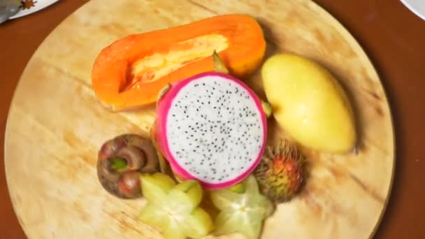 Exotické ovoce na stole. 4k, pohled shora, zpomalené. karamboly a dračí ovoce, papája, mango, mangostanu a longan, mučenka, ovocný plod rozřezaný na kousky, otočit na prkně — Stock video