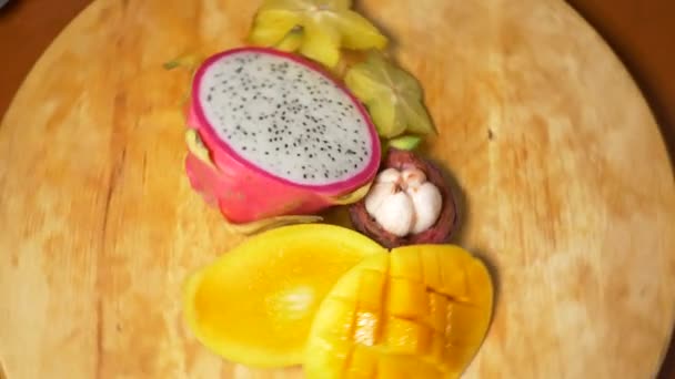 Frutas exóticas en la mesa. 4k, carambola y fruta de dragón, mango, mangostán, fruta de la pasión, fruta cortada en trozos, rotar en una tabla de cortar — Vídeos de Stock