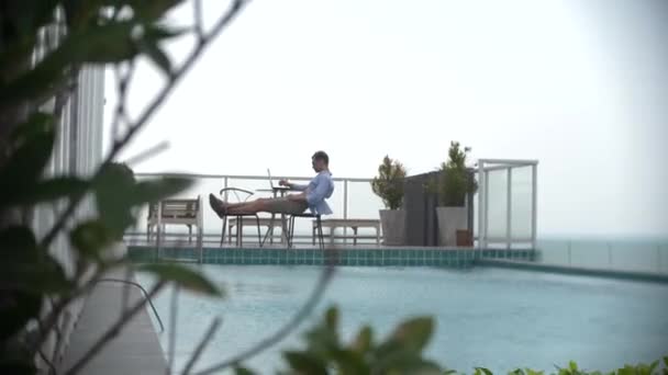 Affärsman med laptop vid poolen på taket med utsikt över havet. gör bakgrunden oskarp — Stockvideo