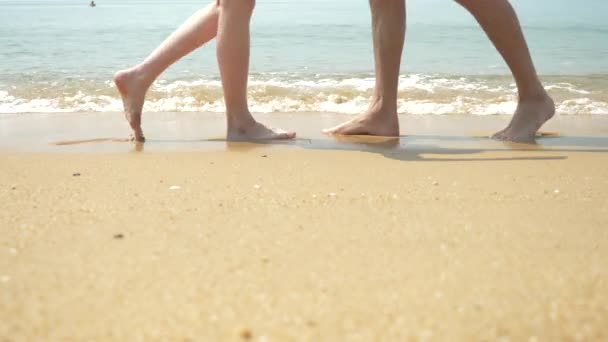 Een paar is een wandeling langs het strand op een heldere zonnige dag. ze houden handen en kus. de voeten van de mannen en vrouwen lopen langs de kust. 4k, slow-motion — Stockvideo