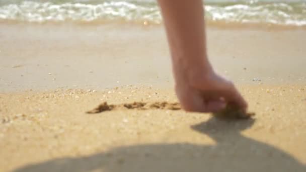 Una mano femenina dibuja un corazón sobre arena mojada. 4k cámara lenta — Vídeo de stock
