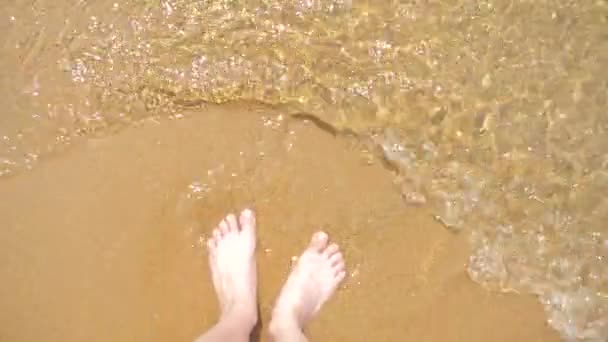 Pés femininos na areia, a onda do mar cobre as pernas femininas. 4k, câmera lenta — Vídeo de Stock