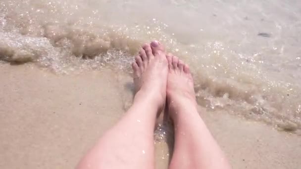 Pés femininos na areia, a onda do mar cobre as pernas femininas. 4k, câmera lenta — Vídeo de Stock