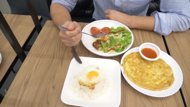 Cozinha tailandesa - arroz, omelete, verduras com o porco. Um homem come comida tailandesa num restaurante. 4k, câmera lenta — Vídeo de Stock