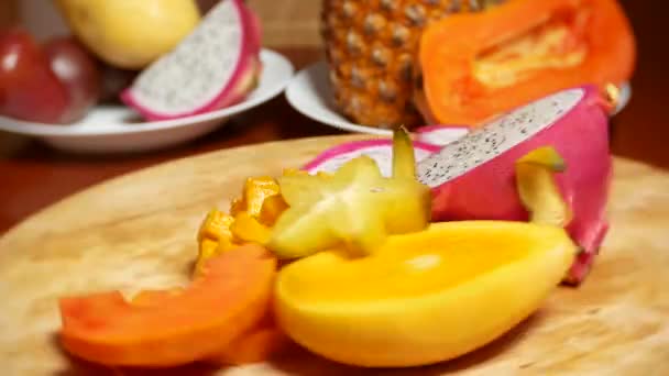 Екзотичні фрукти на столі. 4k, карамбола і дракон фрукти, папайя, манго, манго, манго та довгаста, фрукти пристрасті, нарізані шматочками, обертаються на ріжучій дошці — стокове відео