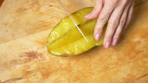 Frutas exóticas en la mesa. 4k, las manos femeninas cortan una carambola con un cuchillo en una tabla de cortar, cámara lenta — Vídeos de Stock