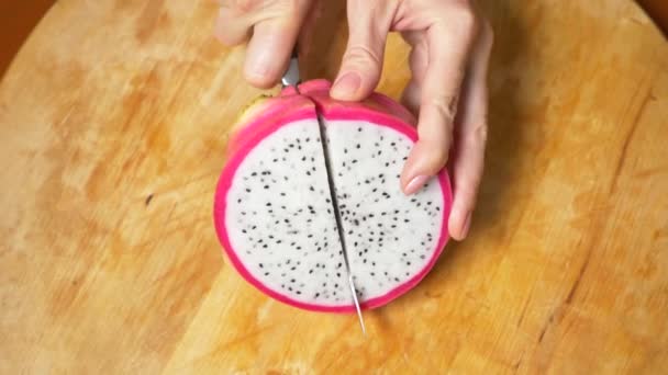 Exotische Früchte auf dem Tisch. 4k, weibliche Hände schneiden eine Drachenfrucht mit einem Messer auf einem Schneidebrett in Stücke — Stockvideo