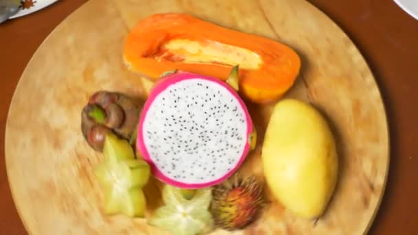 Exotische vruchten op de tafel. 4 k, carambola's en dragon fruit, papaya, mango, Mangostan en longan, passievrucht, fruit, snijd in stukjes, draaien op een snijplank — Stockvideo