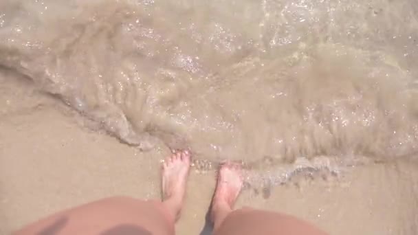 Pés femininos na areia, a onda do mar cobre as pernas femininas. 4k, câmera lenta — Vídeo de Stock