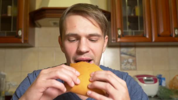 Een man eet een appel strudel met plezier, zittend in zijn keuken. 4k, slow-motion — Stockvideo