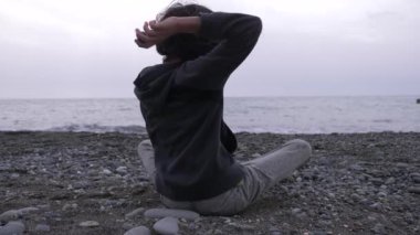 Yalnız bir çocuk kıyıda oturur ve denize taş atar. 4k, ağır çekim