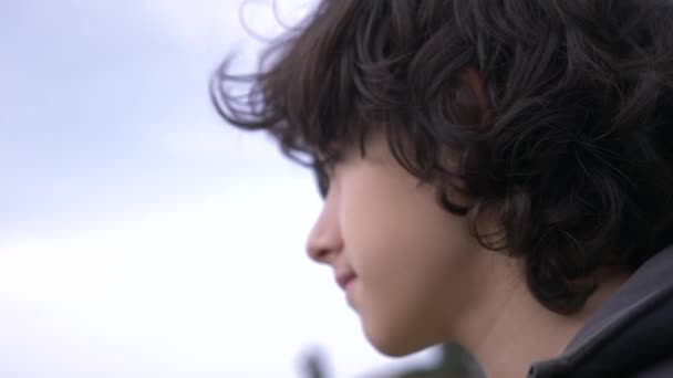 Adolescente bonito com cabelo encaracolado contra o céu azul 4k, tiro em câmera lenta — Vídeo de Stock