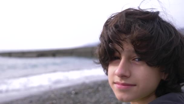Un adolescent mignon aux cheveux bouclés sur fond de mer. 4k, au ralenti — Video