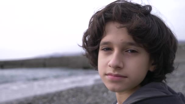 Um adolescente bonito com cabelo encaracolado contra o pano de fundo do mar. 4k, câmera lenta — Vídeo de Stock