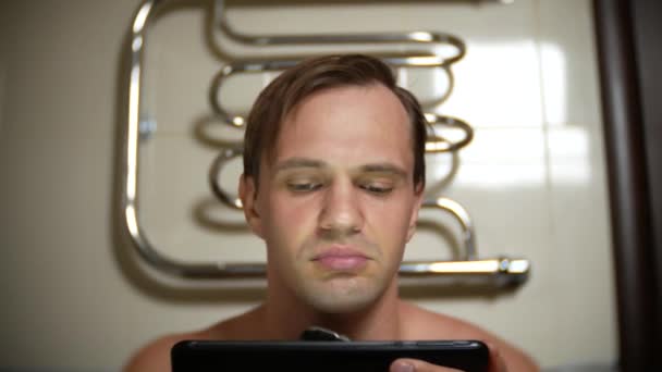 Ansigtet af en mand, der sidder i toilettet og barberer sig med en elektrisk barbermaskine. 4k, nærbillede – Stock-video