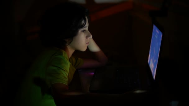 Niño utiliza un ordenador portátil en una habitación oscura, 4k , — Vídeos de Stock