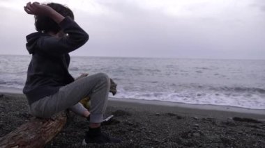 Yalnız bir çocuk kıyıda oturur ve denize taş atar. 4k, ağır çekim