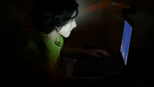 Niño utiliza un ordenador portátil en una habitación oscura, 4k , — Vídeos de Stock