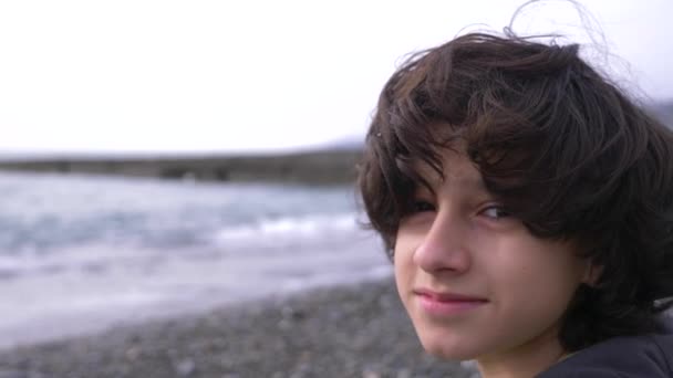 A cute teenager with curly hair against the backdrop of the sea. 4k, slow motion — Stock Video
