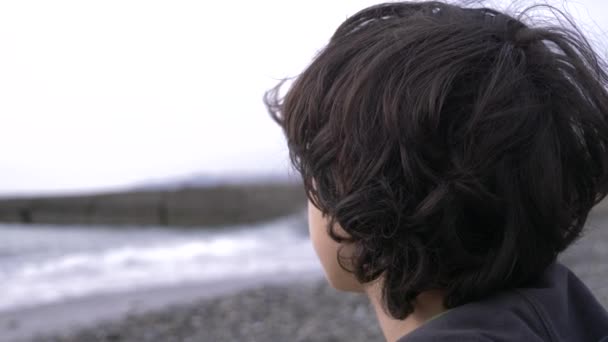 Un adolescent mignon aux cheveux bouclés sur fond de mer. 4k, au ralenti — Video