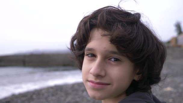 Un adolescent mignon aux cheveux bouclés sur fond de mer. 4k, au ralenti — Video