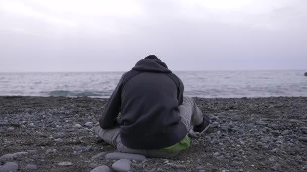 Un chico solitario está sentado en la playa. 4k, cámara lenta — Vídeo de stock
