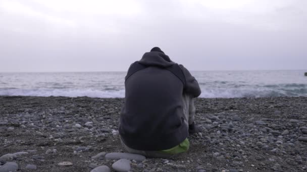 Un ragazzo solo è seduto sulla spiaggia. 4k, rallentatore — Video Stock