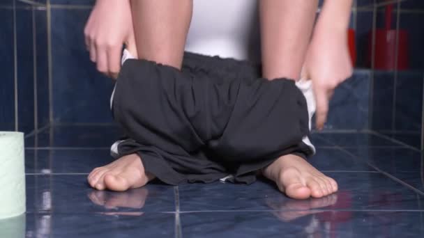 Fötterna på en man som sitter i toaletten med en smärta i magen. 4 k, närbild, killen tonåringen i shorts i toaletten. — Stockvideo