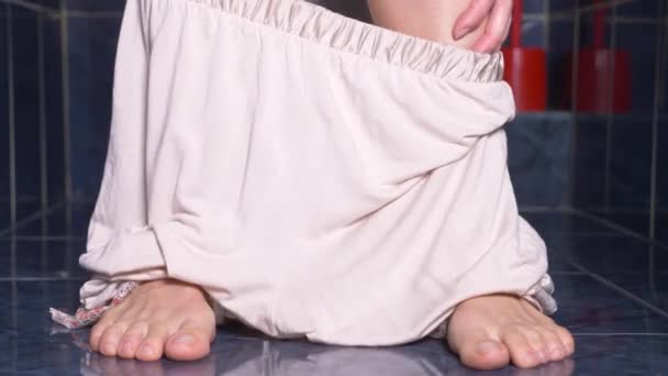 Los pies de un hombre que se sienta en el inodoro con un dolor en el estómago. 4k, primer plano, mujer en pijama en el inodoro — Vídeo de stock
