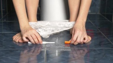 Yakın çekim. onun elinde bir hamilelik testi ile bir tuvalet üzerinde oturan bir bayan. 4k, kadın ayakları