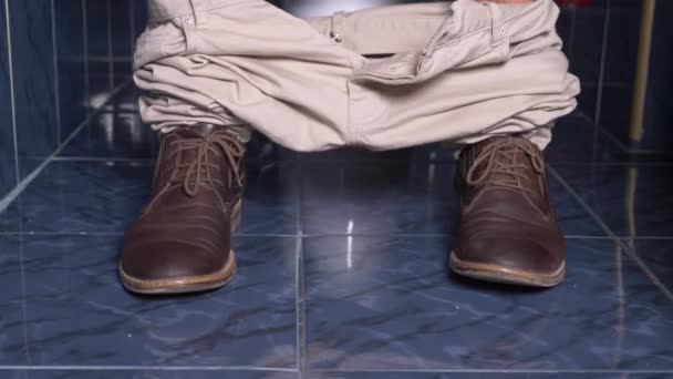 Fötterna på en man som sitter i toaletten med en smärta i magen. 4 k, närbild, mannen i byxor och skor i toaletten — Stockvideo