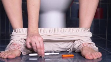 Yakın çekim. onun elinde bir hamilelik testi ile bir tuvalet üzerinde oturan bir bayan. 4k, kadın ayakları