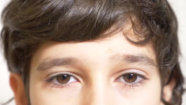 Коричневые глаза мальчика с длинными черными ресницами. он смотрит из-под длинного кудрявого чела. 4к, замедленная съемка, крупный план — стоковое видео